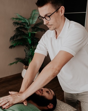 An osteopath treats the neck of a bearded man lying on a table