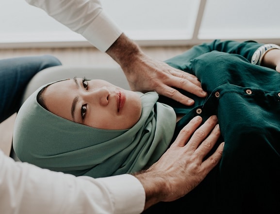 An osteopath's hands rest on the ribcage of a woman lying down