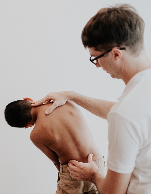 An osteopath examines the spine of a standing boy from behind