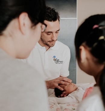 An osteopath gently treats a newborn baby as parents watch