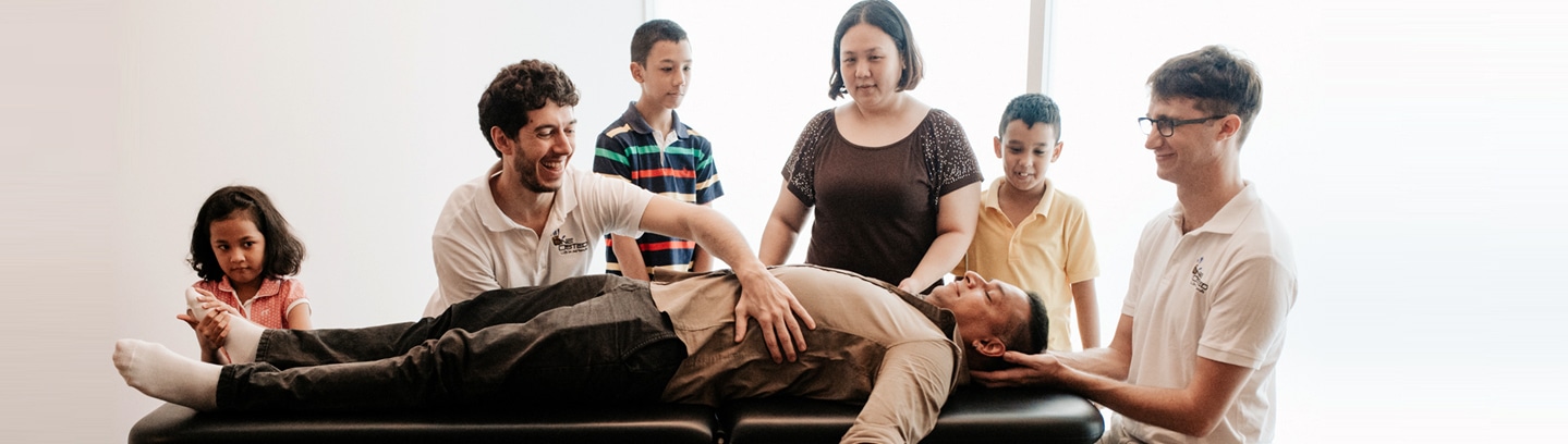 An osteopath treats a man on a table as his family watches
