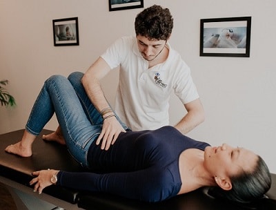 An osteopath treats the lower abdomen of a woman lying with knees bent