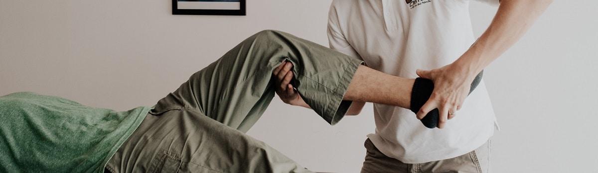 An osteopath mobilises the bent knee of a patient lying down