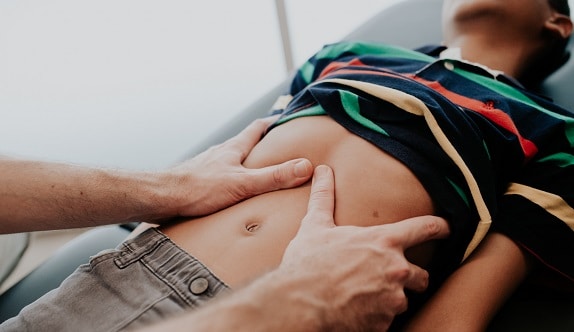 An osteopath palpates the abdomen of a child lying down