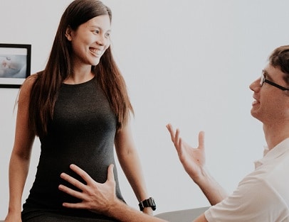 An osteopath talks with a smiling pregnant woman seated on a treatment table