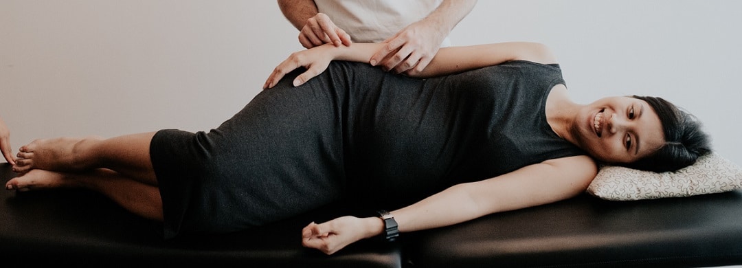 An osteopath treats the hip of a smiling woman lying on her side