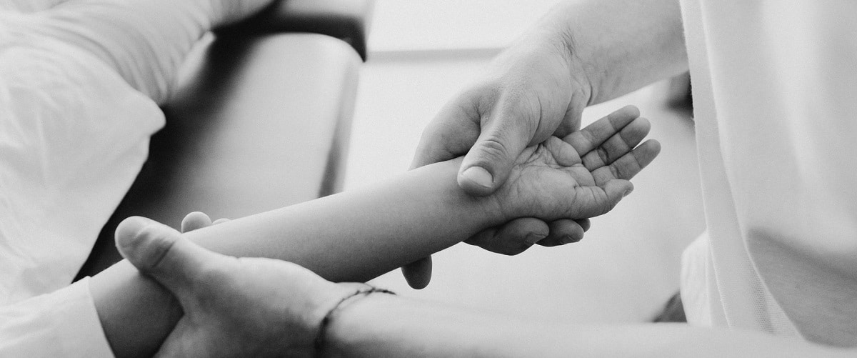 An osteopath's hands support a child's forearm and open hand, in black and white