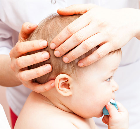 Baby treating by an osteopath, hands on his head